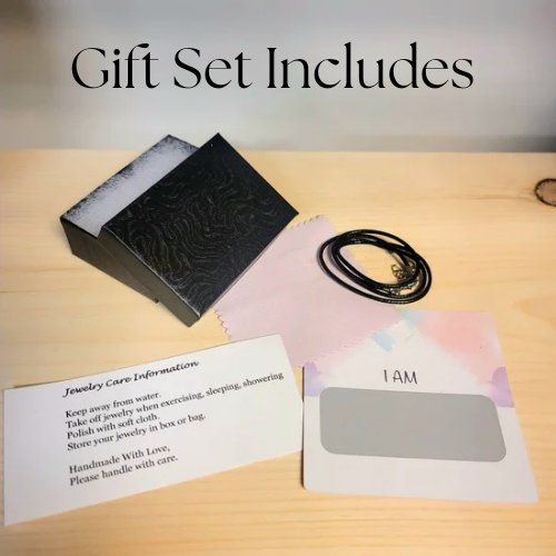 Alisa Marie Gift Set Includes: Black embossed jewelry box, black cord necklace, jewelry care information card with handling instructions, and 'I AM' affirmation card on wooden surface.
