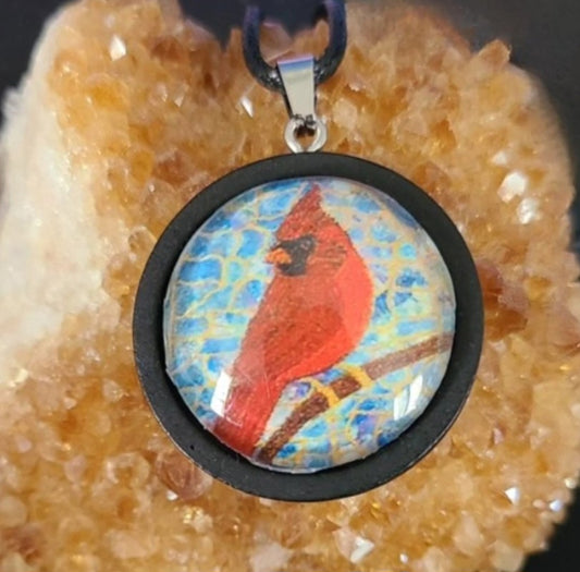 Alisa Marie original artwork, Always Beside You, Cardinal Memorial Pendant featuring a red cardinal bird in black wooden frame design on turquoise blue background, displayed on citrine crystal with black cord.