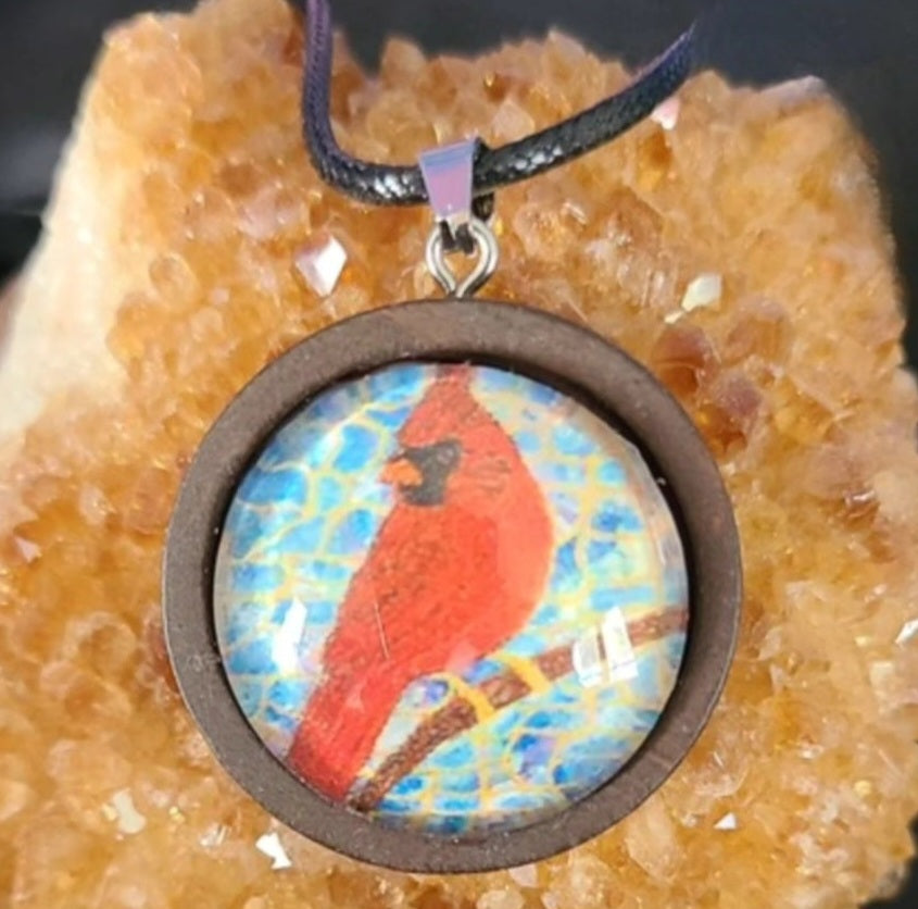 Alisa Marie original artwork, Always Beside You, Cardinal Memorial Pendant featuring a red cardinal bird in brown wooden frame design on turquoise blue background, displayed on citrine crystal with black cord.