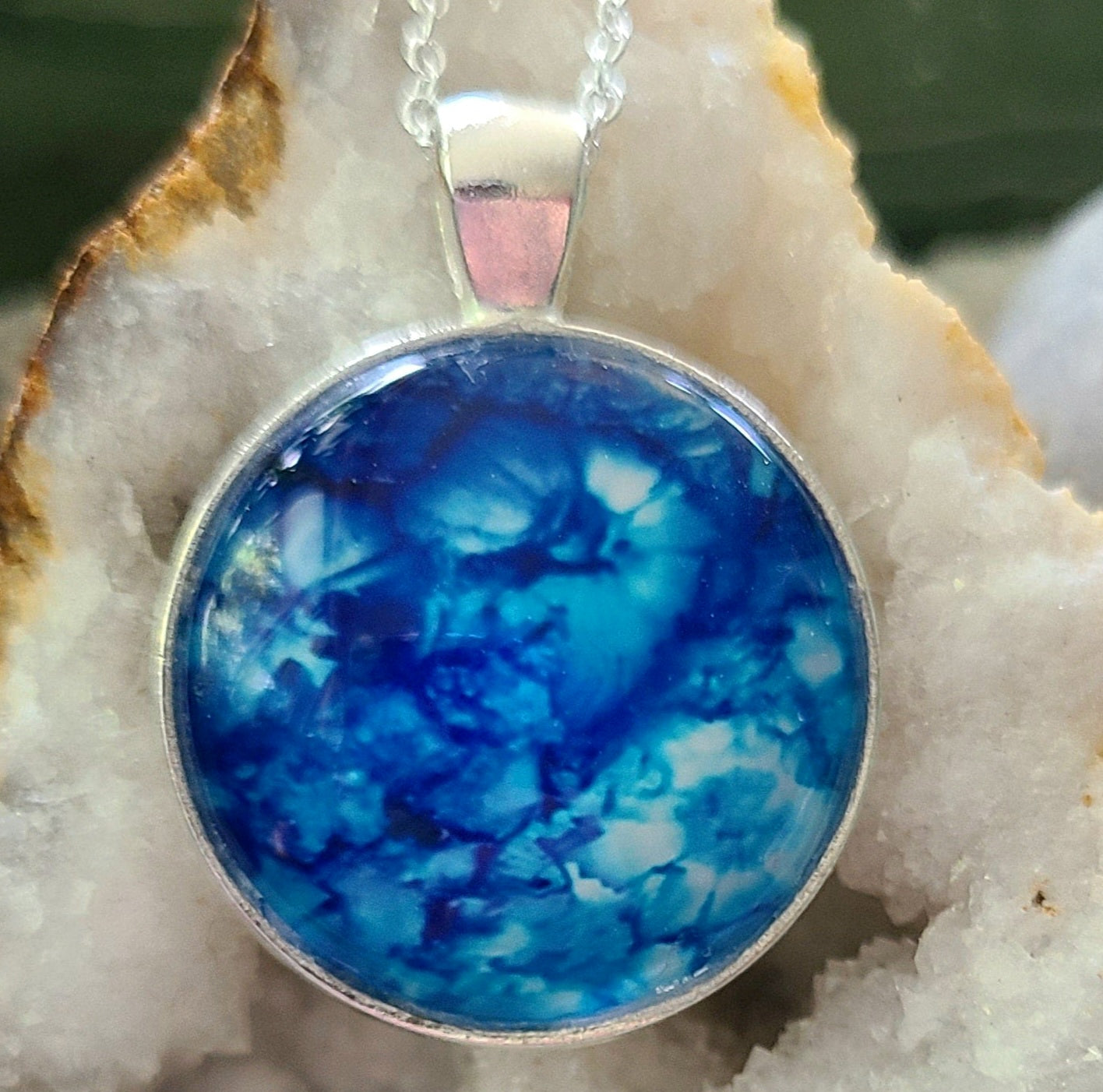 Alisa Marie original artwork, Serenity pendant featuring deep ocean blue tones, set in silver frame with silver chain, displayed on white crystal geode.