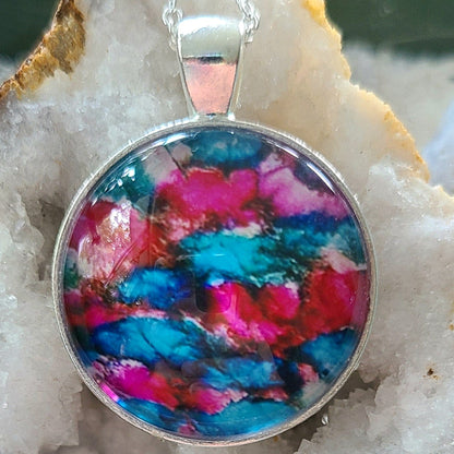 Alisa Marie original artwork, Blue Roses pendant featuring shimmering magenta, blue and white tones, set in silver frame with silver chain, displayed on white crystal geode.