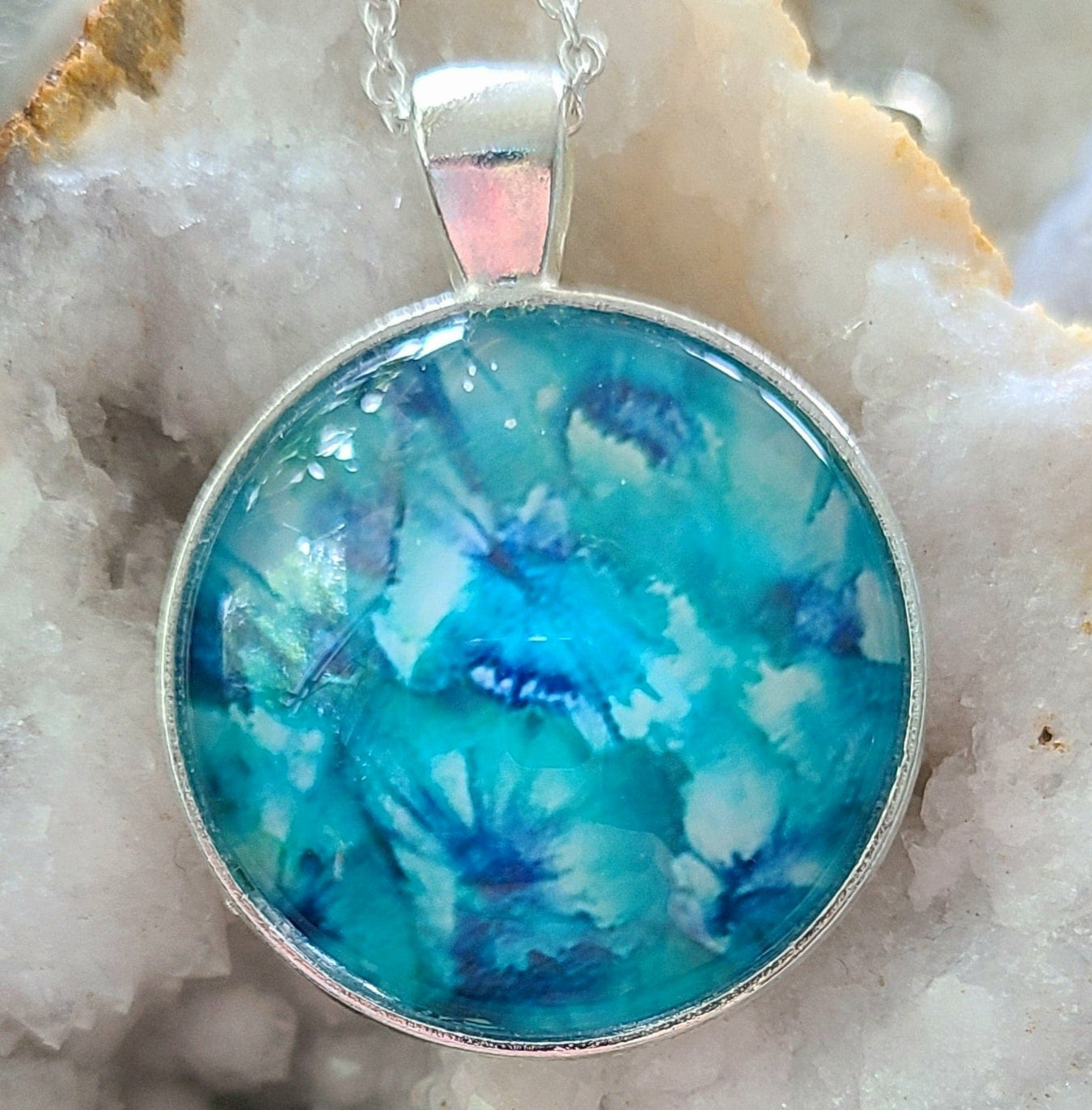 Alisa Marie original artwork. Sea Glass pendant featuring vibrant aqua and turquoise tones, set in silver frame with silver chain, displayed on white crystal geode.
