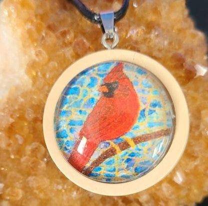 Alisa Marie original artwork, Always Beside You, Cardinal Memorial Pendant featuring a red cardinal bird set in natural wooden frame on turquoise blue background, displayed on citrine crystal with black cord.