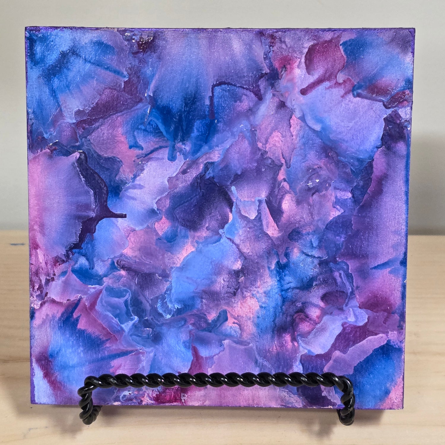 Abstract art piece with a textured surface and black cord on a light wood background